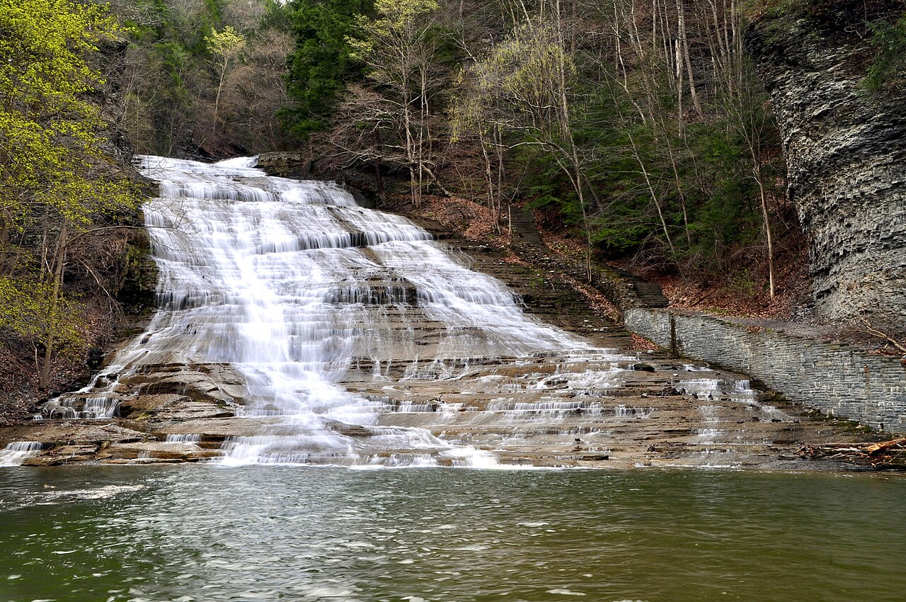 Buttermilk Falls streaming down a broad stepped rock face into a pool at Buttermilk Falls State Park in early spring.