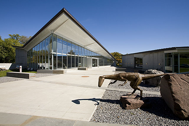 The glass-fronted entrance of the Museum of the Earth in Ithaca with a bronze Coelophysis sculpture outside.