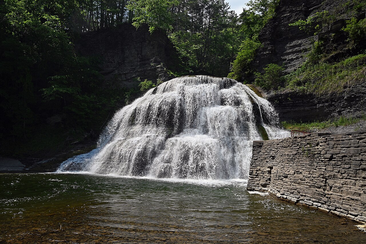 The Lower Falls of Enfield Glen in Robert H. Treman State Park spilling into a green swimming hole below wooded cliffs.